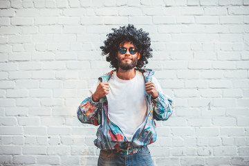 Stylish young man in a retro jacket. Fashion trends of 90s. Handsome hipster guy with beard with curly hair. - obrazy, fototapety, plakaty