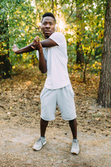 Athletic African-American man doing stretching exercises, preparing for morning workout in the Park