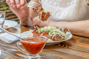 Woman eating barbecue in a cafe. Female hands close-up holding a fork with a piece of barbecue