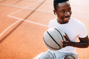 Sporty African American resting after a workout sitting on the court with a basketball, basketball player