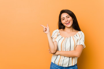 Young curvy woman smiling cheerfully pointing with forefinger away.