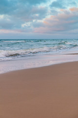 Fototapeta na wymiar sandy beach by the turquoise sea in cloudy weather in sunset light