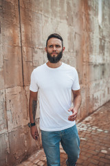 Obraz premium Handsome hipster man with beard wearing white blank t-shirt with space for your logo or design. white t shirt mockup.