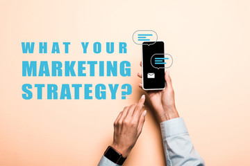 cropped view of woman pointing with finger at smartphone with what your marketing strategy lettering on pink