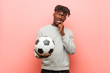 Young fitness black man holding a soccer ball relaxed thinking about something looking at a copy...