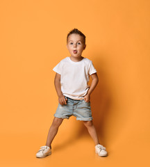 Kid boy bully in white t-shirt and blue jeans shorts is sticking out his tongue teasing us on yellow