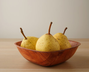 Three yellow garden ripe pears in a red bamboo bowl on the table with copy space, selective focus