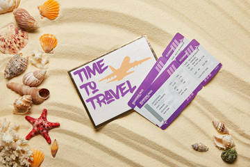 top view of card with time to travel letting near air tickets and seashells on sandy beach