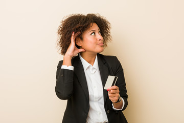 Young african american woman holding a credit card trying to listening a gossip.