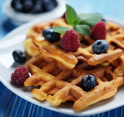 Traditional belgian waffles with fresh berrys and sugar powder on white plate, blue wooden background.