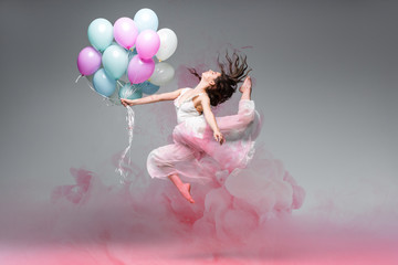 beautiful ballerina dancing with festive balloons near pink smoke splashes on grey background © LIGHTFIELD STUDIOS