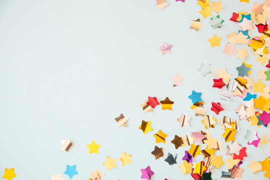 Color Stars Confetti On Light Blue Background. Festive, Party Or Holiday Glowing Backdrop. Flat Lay, Top View.