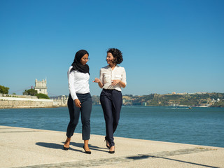 Female office friends walking outside and chatting. Muslim businesswoman and her colleague going...
