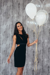 Cute brunette woman standing smiling and playing with balloons.