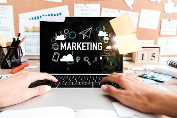 cropped view of woman using laptop with marketing lettering on screen near sticky notes