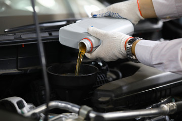 Focus on auto mechanic in gloves replacing and pouring fresh oil into engine at automobile service...