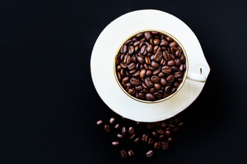 White cup of roasted coffee beans on black background