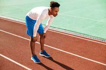 Obraz premium Young tired African American sportsman made a stop during run on racetrack at stadium