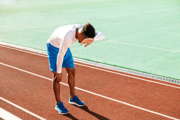 Fototapeta premium Young exhausted African American sportsman made a stop during run on racetrack at stadium