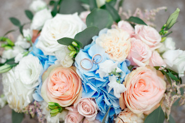 Close-up of bridal diamond wedding band and engagement ring placed in brides floral bouquet