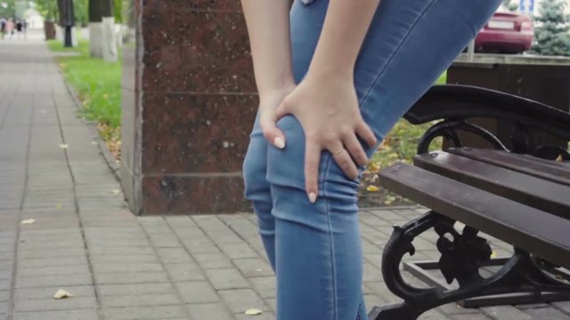 Woman standing up from bench feeling sharp knee pain in park, osteoarthritis, injury