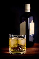WHISKEY GLASS WITH ICE AND BOTTLE ON DARK FUND