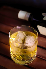 WHISKEY GLASS WITH ICE AND BOTTLE ON DARK FUND