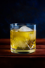 WHISKEY GLASS WITH ICE ON WOODEN TABLE AND BLUE BACKGROUND WITH TEXTURE