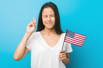 Young hispanic woman holding a united states flag crossing fingers for having luck