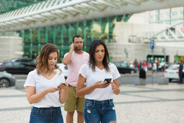 Two women walking on street with phones. Smiling friends holding smartphones while strolling. Communication and technology concept