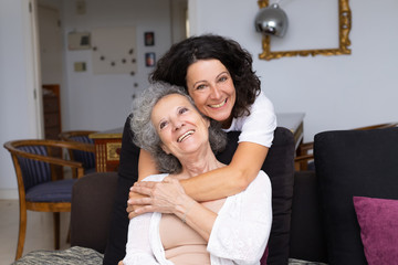 Happy middle aged woman hugging senior lady in living room. Mother and daughter embracing each...