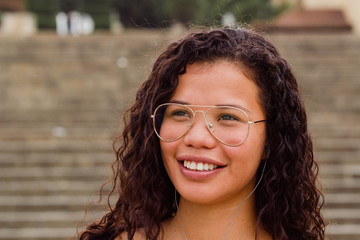 Portrait of a young latin woman listening music and smiling with glasses