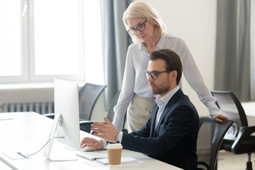 Aged female boss listens young manager asking about task