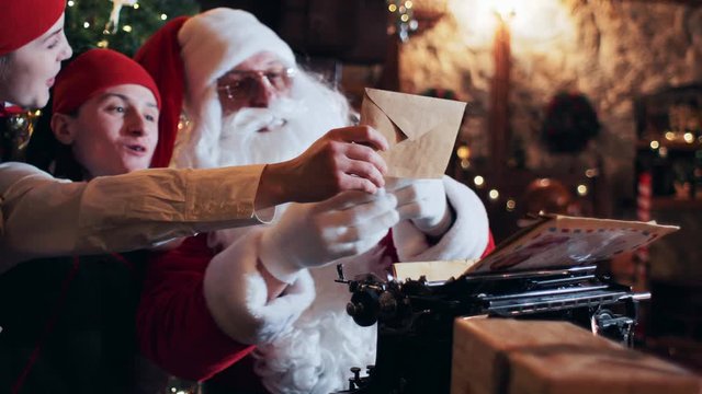 Santa Claus and elves in a residence sitting at a table near a typewriter reading letters