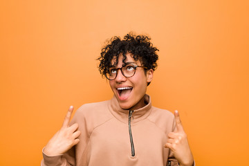 Young mixed african american woman against a brown background indicates with both fore fingers up...