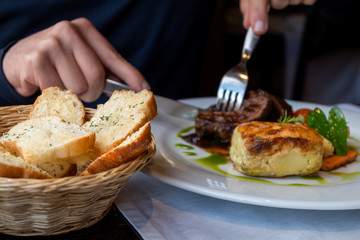 Bread basket and meal. A man is cutting a piece of meat behind. Dinner at a restaurant