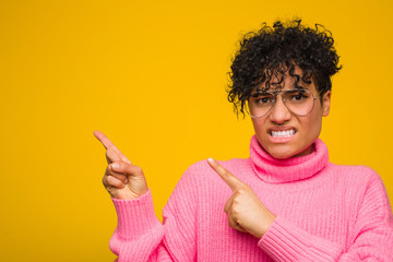 Young african american woman wearing a pink sweater shocked pointing with index fingers to a copy space.