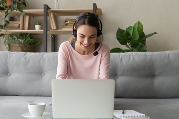 Smiling woman wear wireless headset using laptop at home