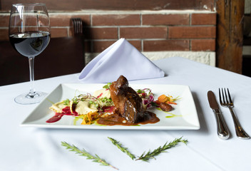 Ravioli with a piece of meat, coloring sauces and a cup of wine on a rustic background with cutlery and a glass of wine