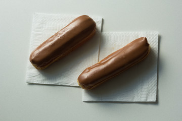Two eclair with chocolate topping on the white napkins on white background