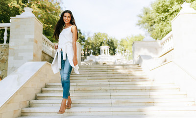 Fototapeta premium Horizontal full view image of beautiful young woman holding disposable cup of coffee in the city street. Pretty female takeaway coffee in hand. Student female drinking coffee outdoor in the morning.