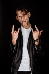 Naklejka premium brutal man sticking out tongue and showing rock sign isolated on black