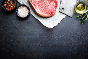 Raw fresh meat Ribeye Steak and seasonings on dark background, top view with copy space
