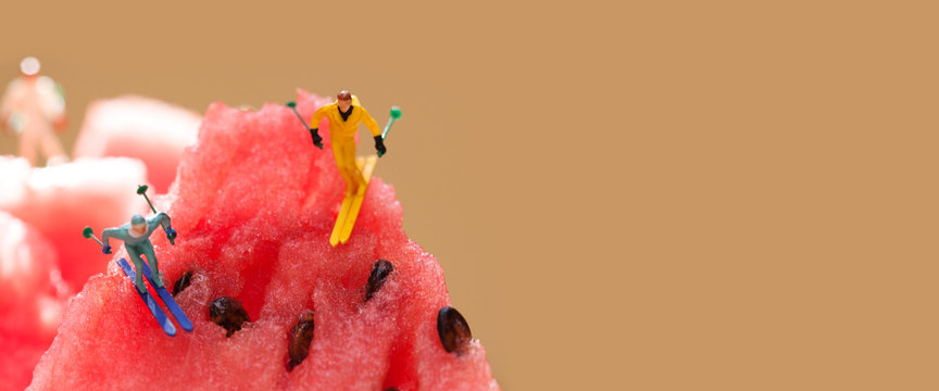 Sport extreme ski slalom concept. Two little skier sportsmans on watermelon mountains. Macro view ripe red watermelon hills landscape, selective focus. brown background copy space