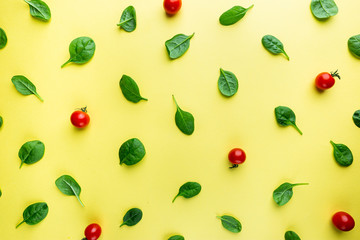 Spinach leaves and tomato pattern background on yellow, top view