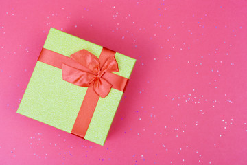 Green gift box with bow on trendy colored background with sparkles. Flat lay style.