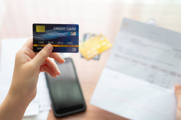 Women hand hold credit card and checking, verify, validate, analysis money transaction with invoice, bills and in the frame include stacked of others credit cards