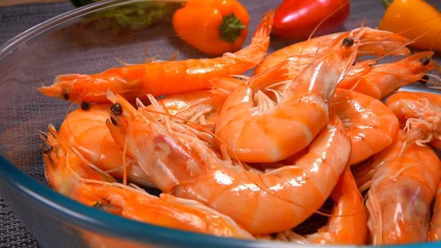 Hand takes delicious large unpeeled shrimp from a glass bowl