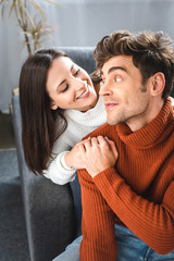 attractive girlfriend and boyfriend in sweaters smiling and hugging in apartment