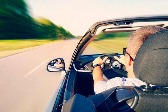 Man Driving A Convertible Car On Country Road. View From Inside Behind The Driver. Man Is Driving At High Speed On The Highway. Dangerous Fast Driving. Motion Blur Effect